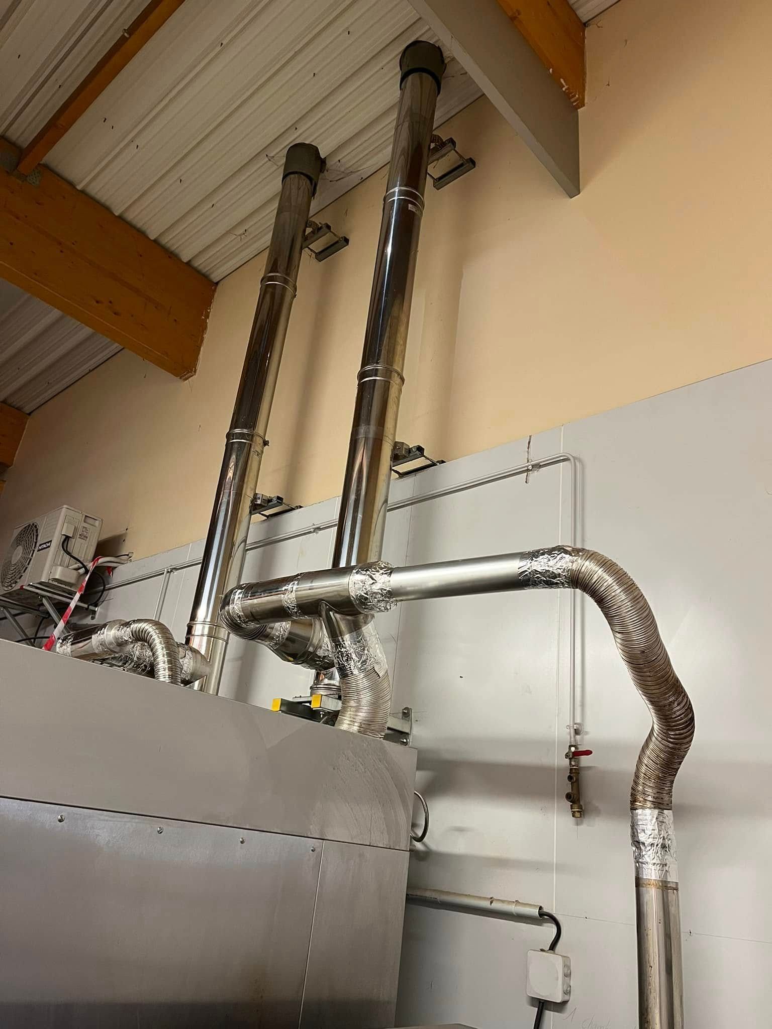 Des conduits de ventilation industriels en acier inoxydable s'élèvent d'une structure métallique vers un plafond clair.