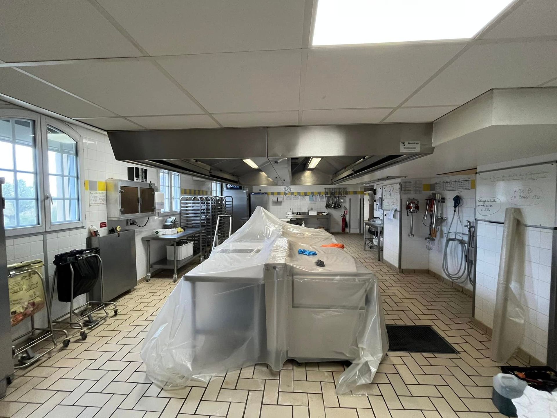 Une cuisine professionnelle avec sol carrelé, équipements en acier inoxydable recouverts de bâches en plastique.