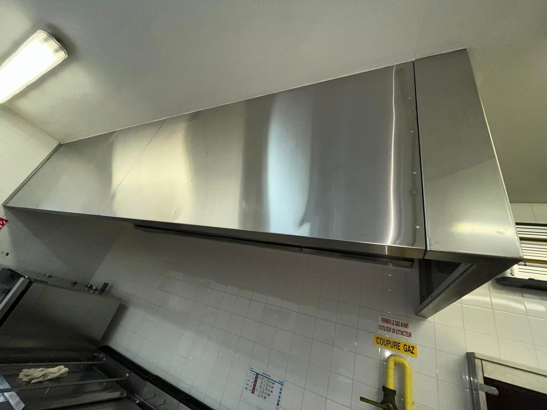 Une hotte aspirante professionnelle en acier inoxydable installée au-dessus d'un mur de cuisine carrelé.