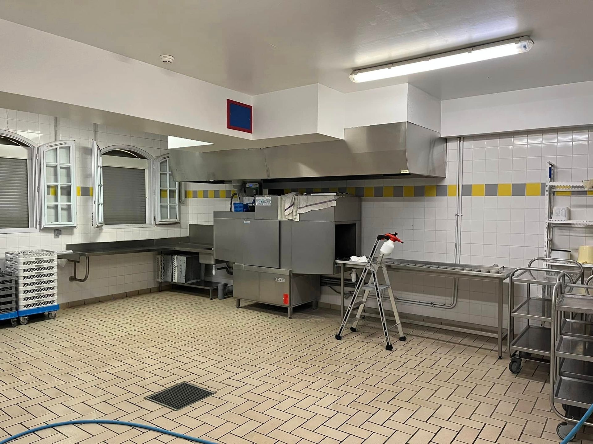 Cuisine professionnelle équipée d'un grand lave-vaisselle en métal sous une hotte aspirante.