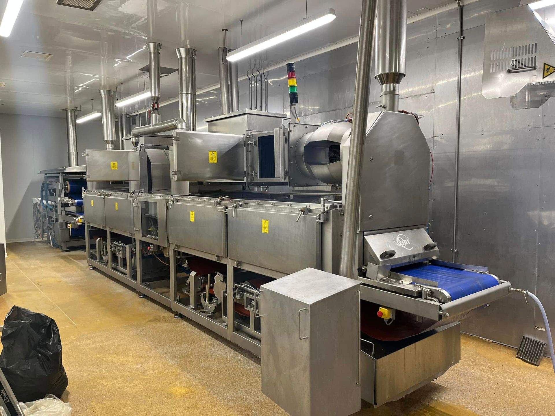 Machine industrielle de transformation alimentaire et tapis roulant bleu, dans une installation propre et lumineuse.