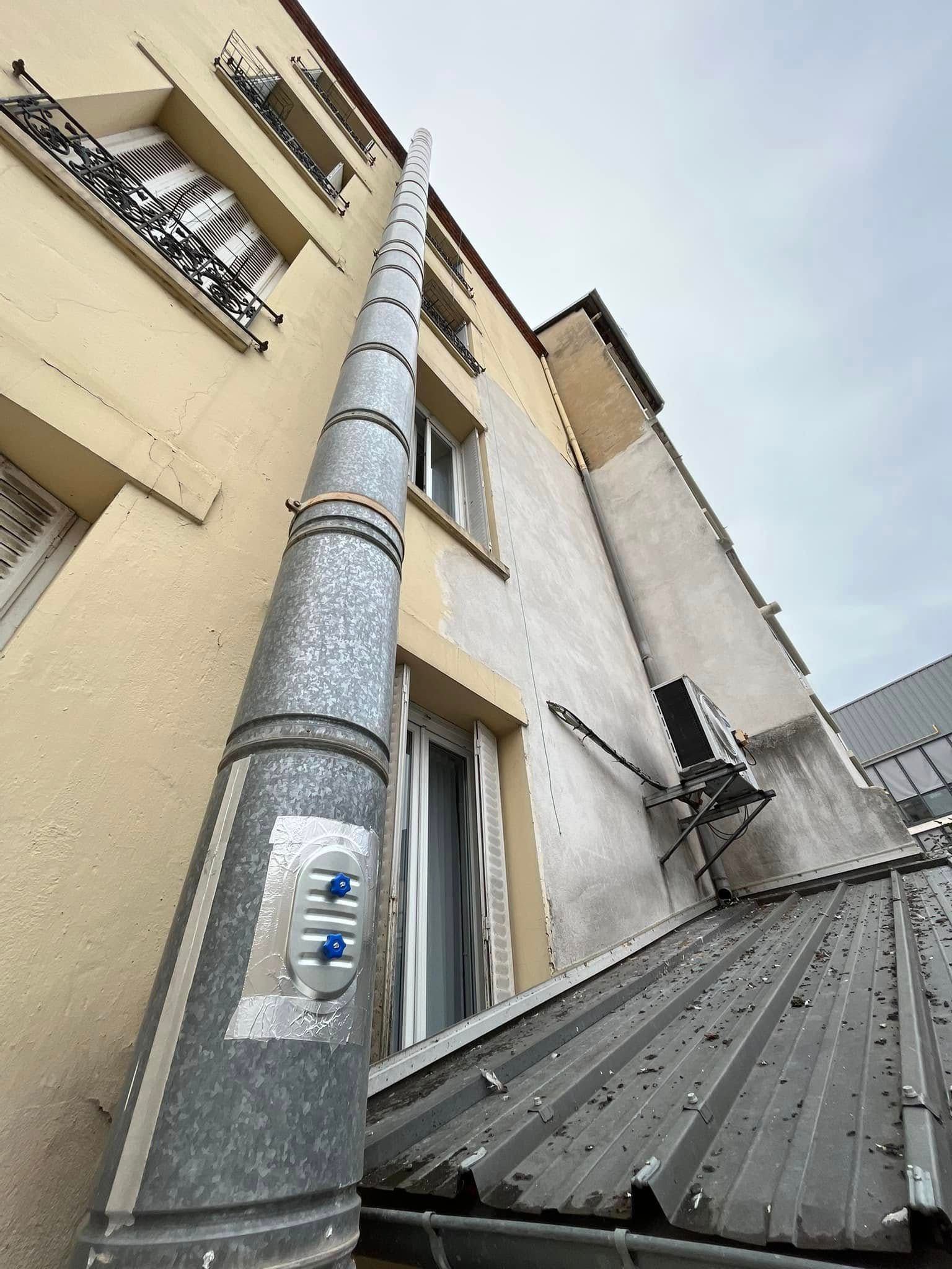 Un grand tuyau de VMC fixé au mur extérieur d'un immeuble à plusieurs étages.