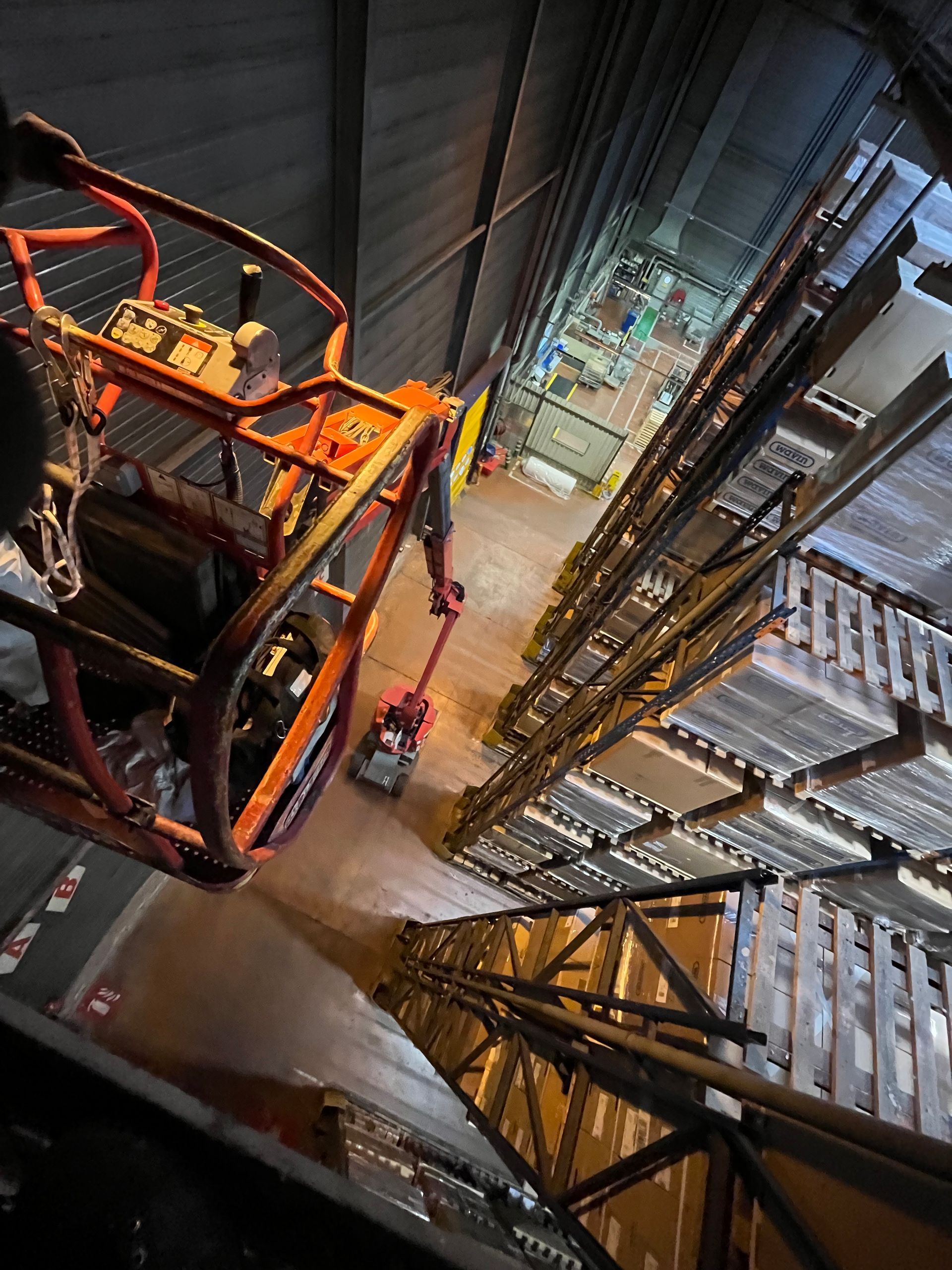 Vue aérienne depuis une nacelle élévatrice sur une allée d'entrepôt avec de hautes étagères de stockage. 