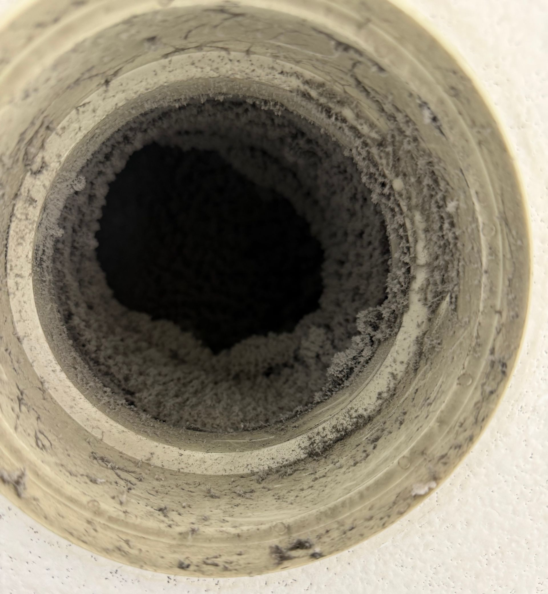 Gros plan sur l'intérieur d'un conduit d'aération circulaire fortement obstrué par une épaisse couche de peluches.