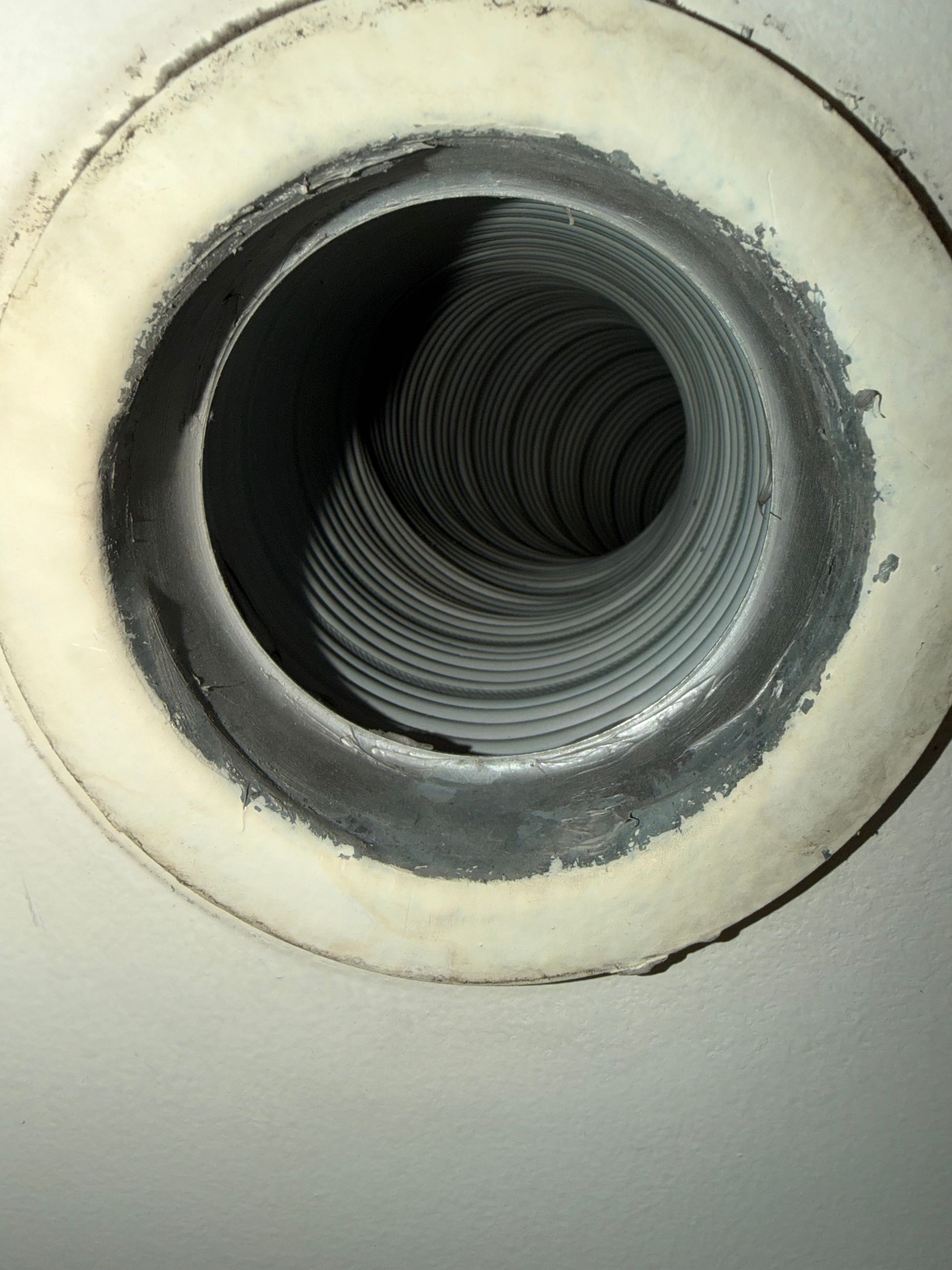Vue intérieure d'un conduit de ventilation circulaire en métal ondulé installé dans un plafond blanc.