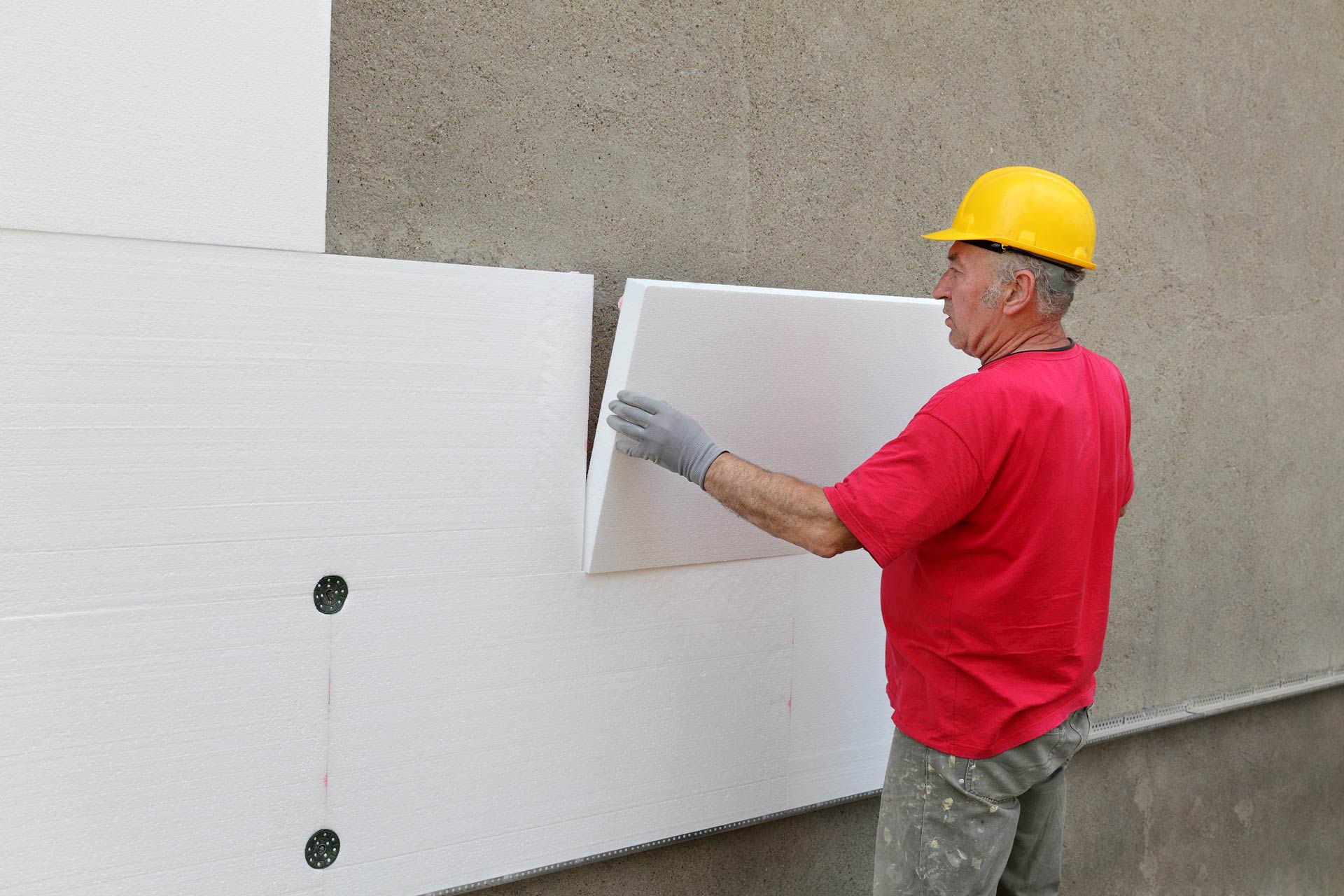 Un ouvrier du bâtiment installe un isolant en mousse sur un mur.