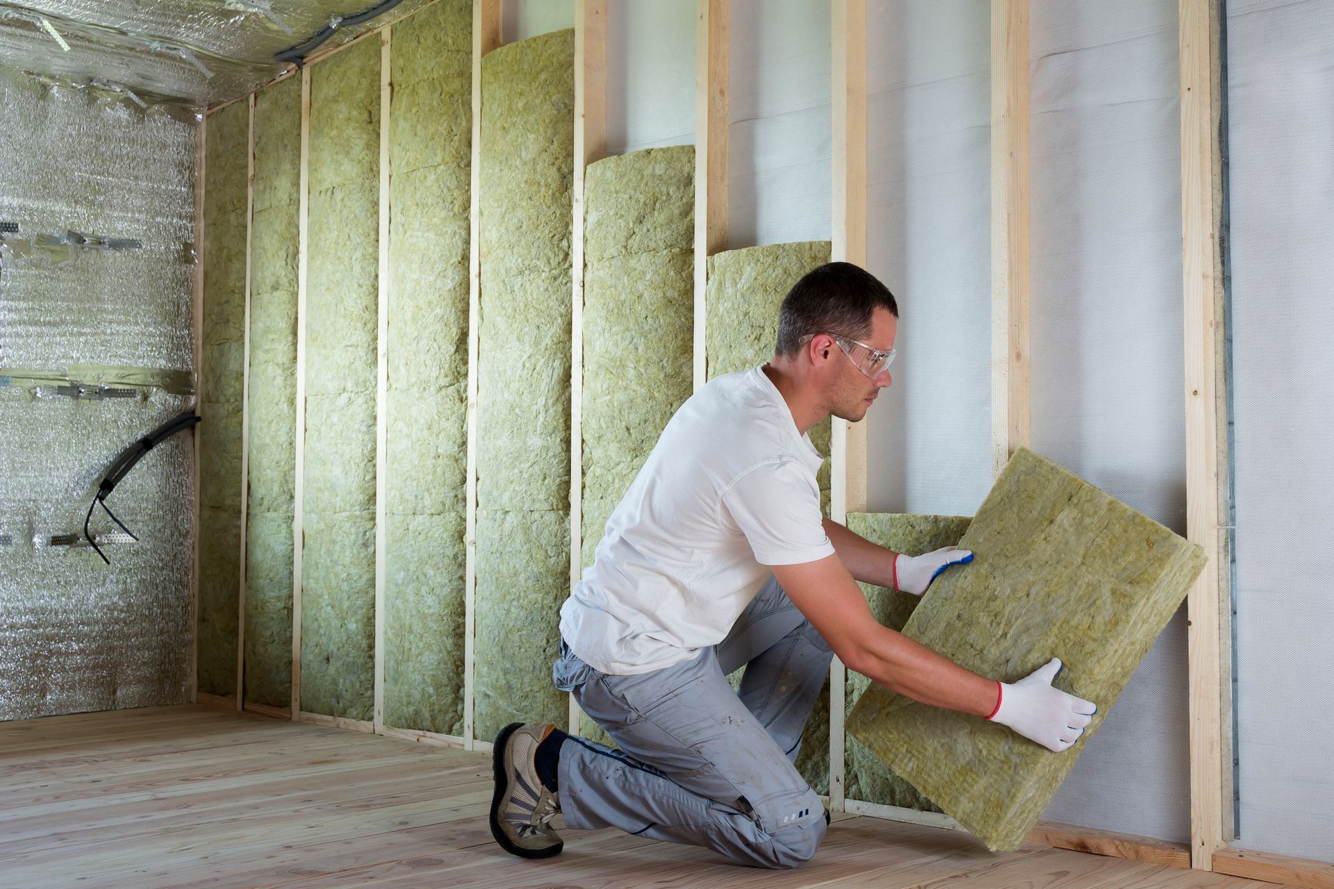 Un homme installe de l'isolant dans un mur ; intérieur, sur un chantier.