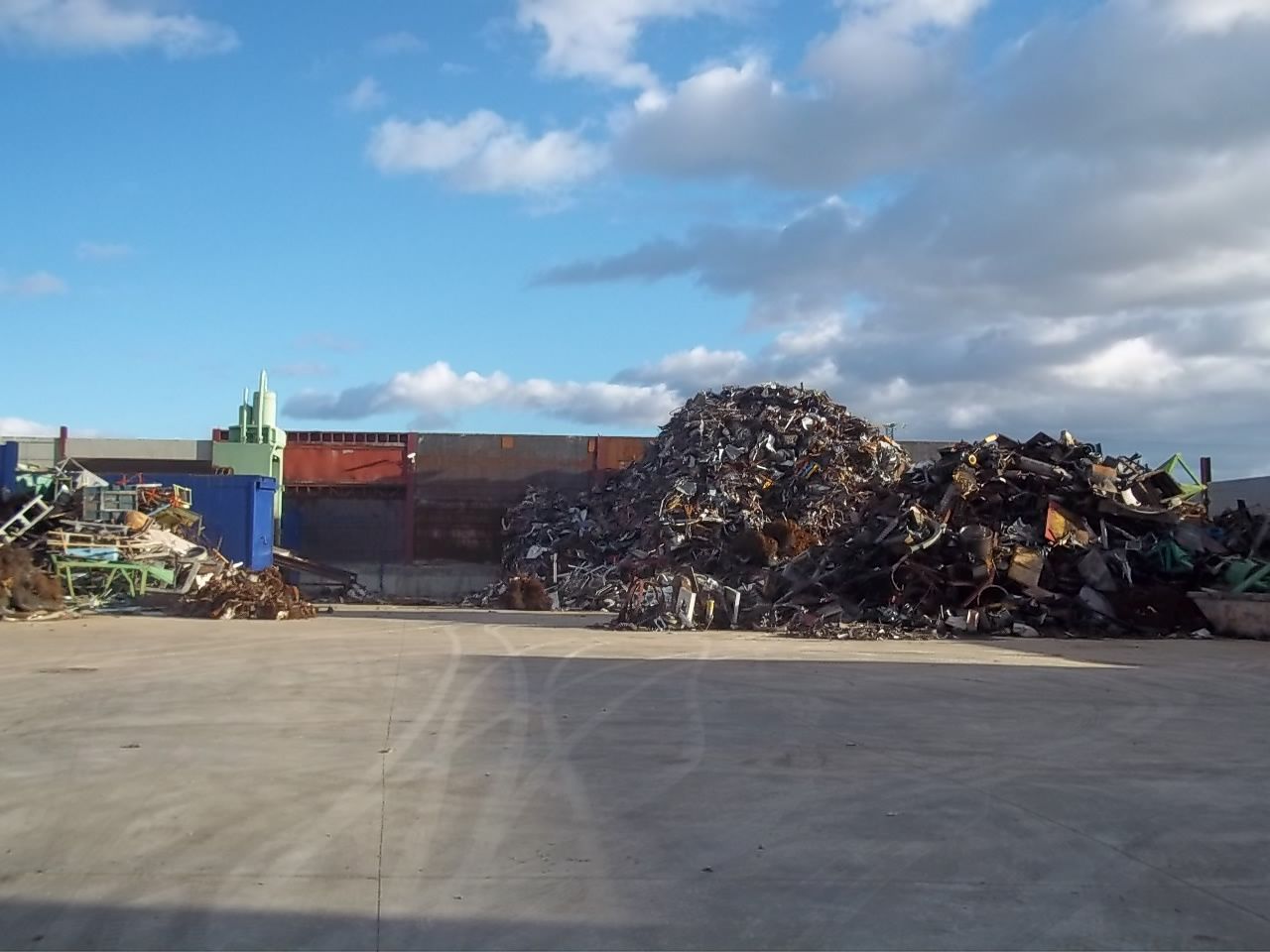 Una gran pila de chatarra en un patio con un edificio azul al fondo.