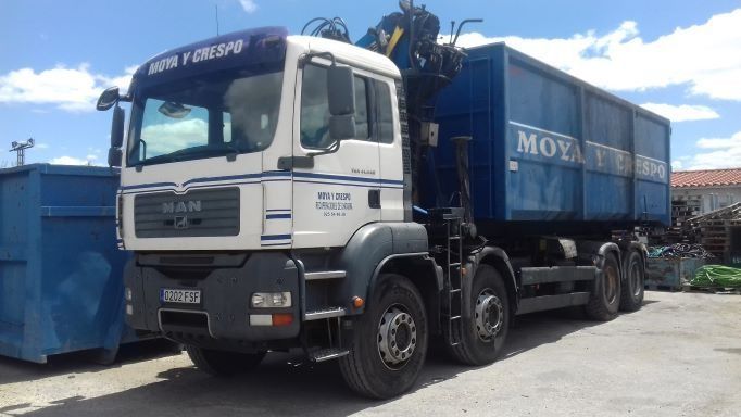 Un camión de reparto está aparcado al lado de un contenedor de basura azul.