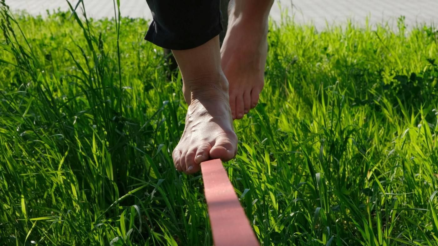 Equilibrio descalzo sobre una cuerda floja sobre hierba verde alta
