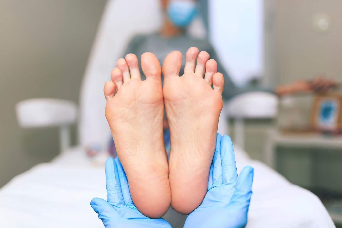 Manos enguantadas de azul sujetando los pies descalzos de una persona sobre una mesa de exploración.