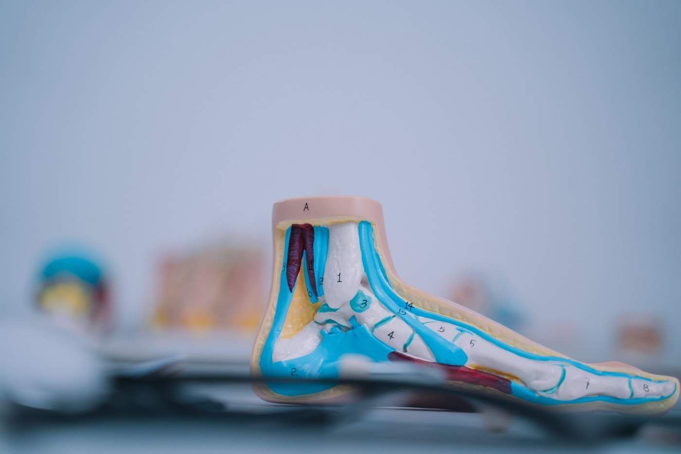 Escultura de zapato de cerámica pintada en azul, blanco y beige sobre una mesa, con una segunda pieza borrosa al fondo.