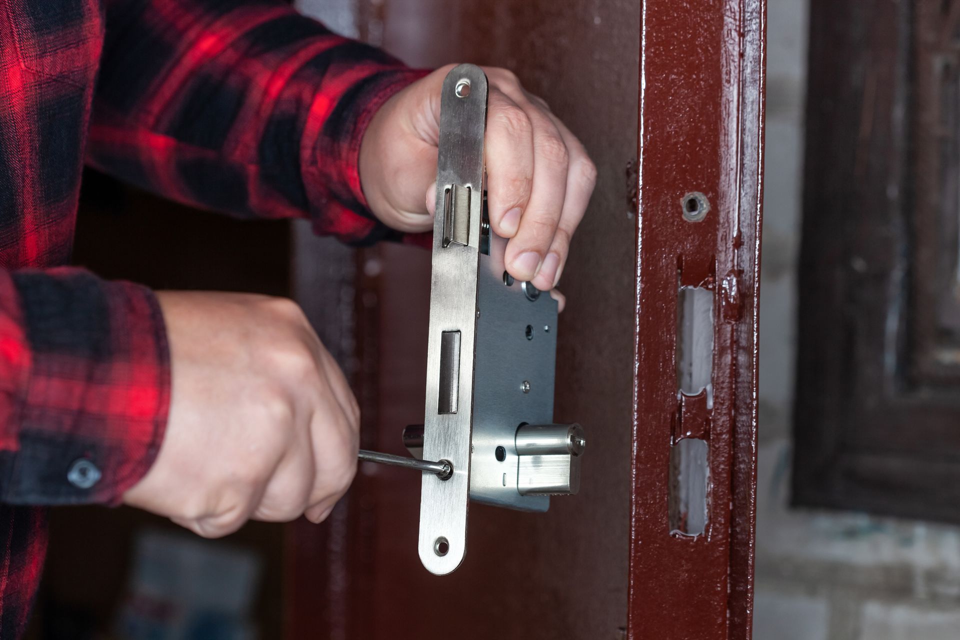 Des mains installent une serrure argentée sur une porte en bois.