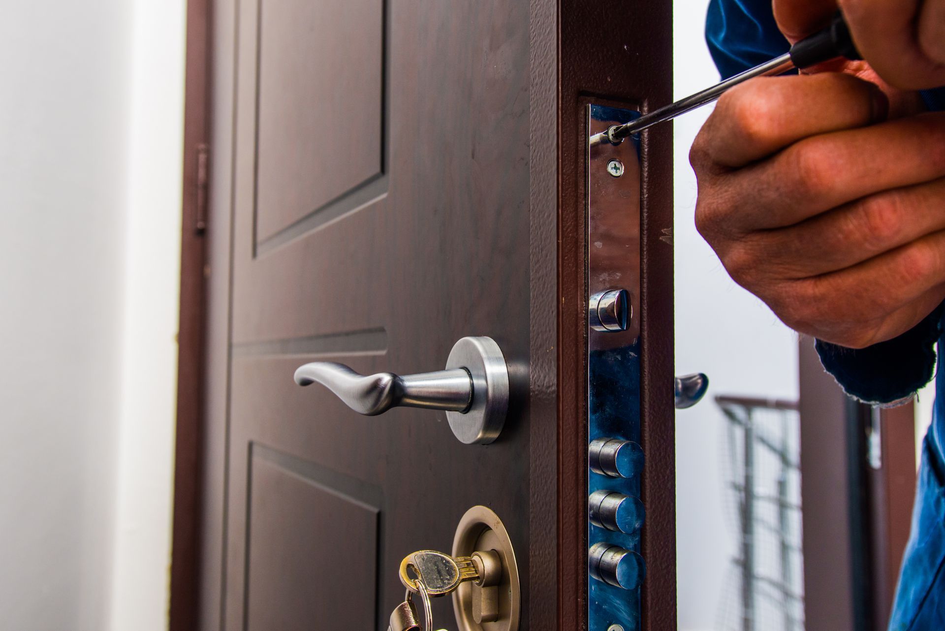 Une main tenant un tournevis près d'une serrure de porte, la porte étant entrouverte.