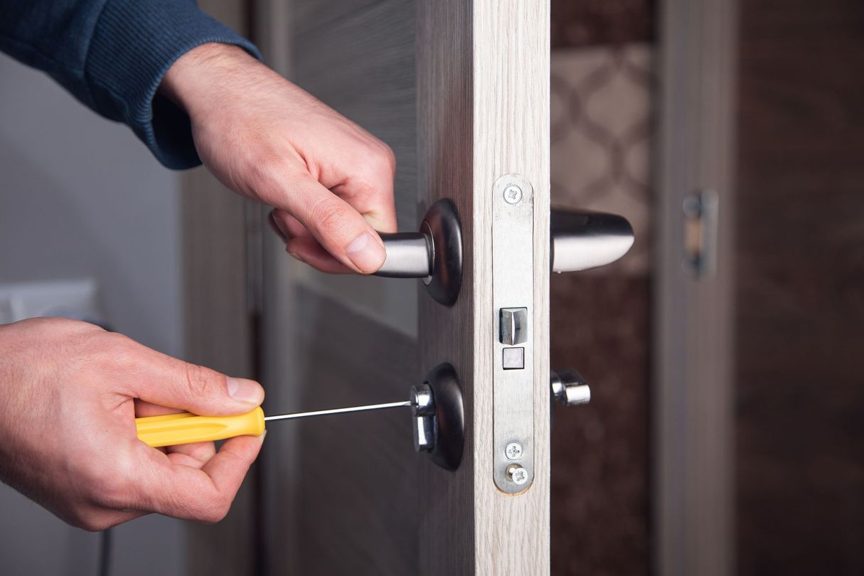 Mains utilisant un tournevis pour retirer une serrure de porte en bois.