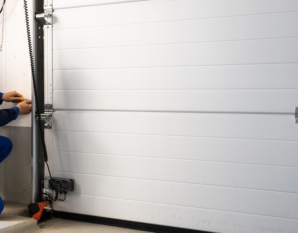 Un technicien en combinaison répare une porte de garage près d'une boîte à outils.