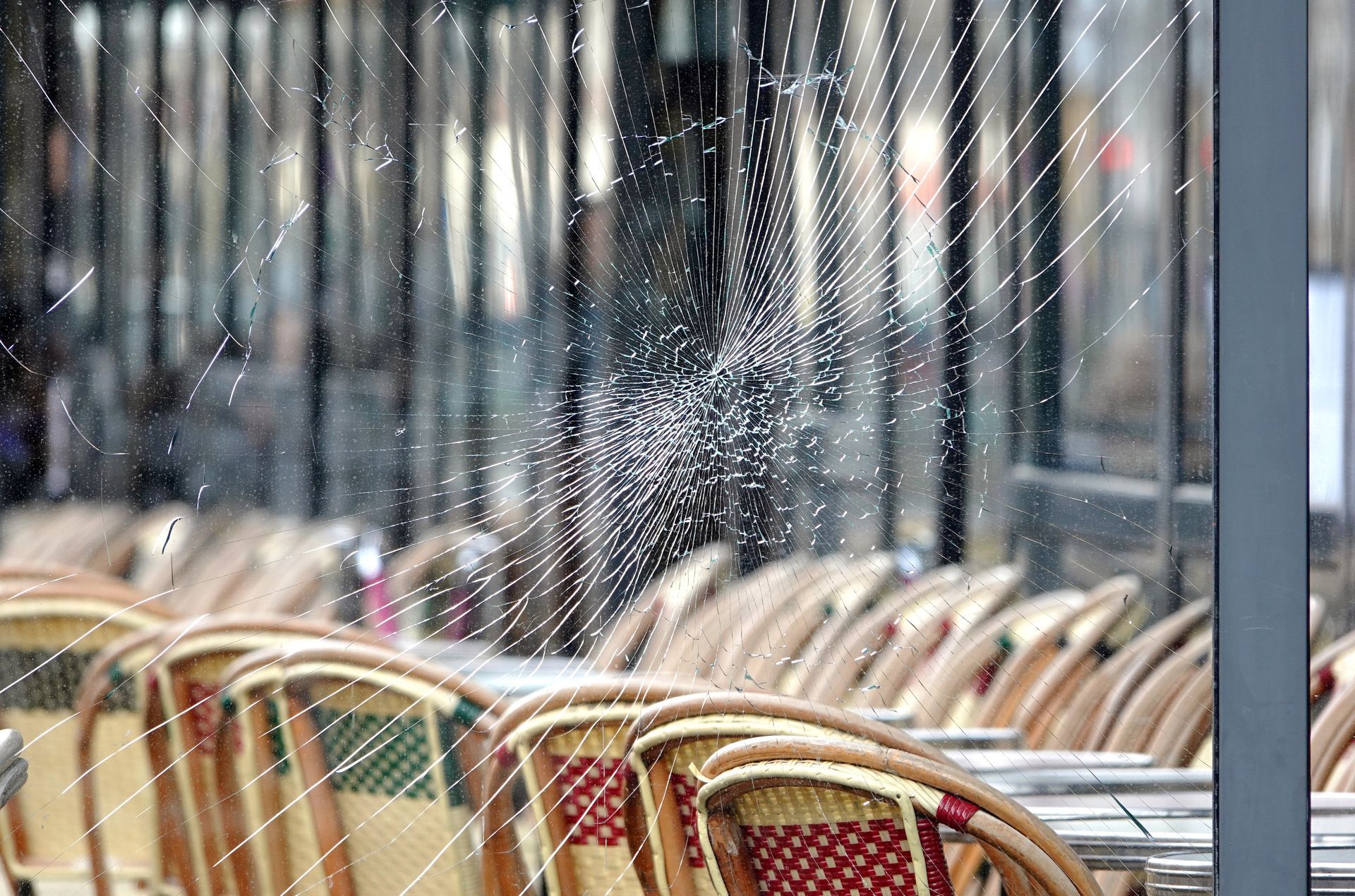 Terrasse de café vide avec des chaises en osier derrière une fenêtre mouchetée de pluie.