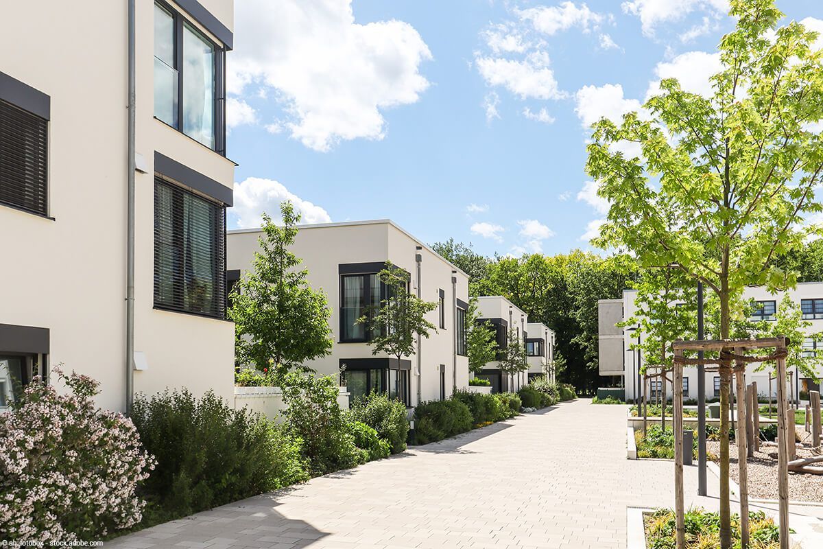 Moderner Apartmenthof mit weißen Gebäuden, Bäumen und einem sonnigen gepflasterten Gehweg