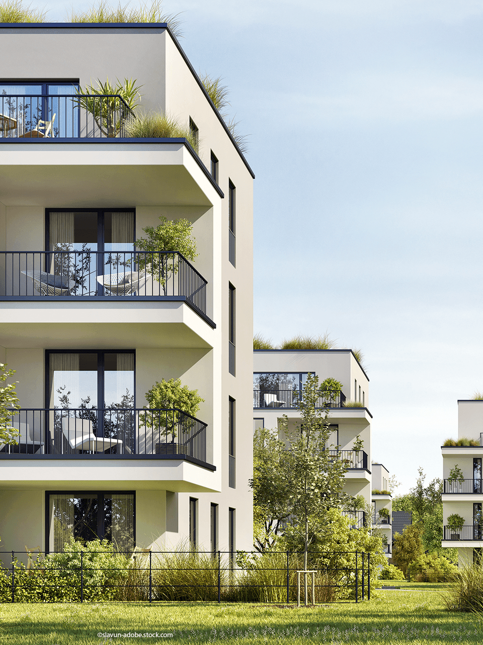 Moderne, weiße Apartmentgebäude mit Balkonen und Grünflächen in einem begrünten Innenhof