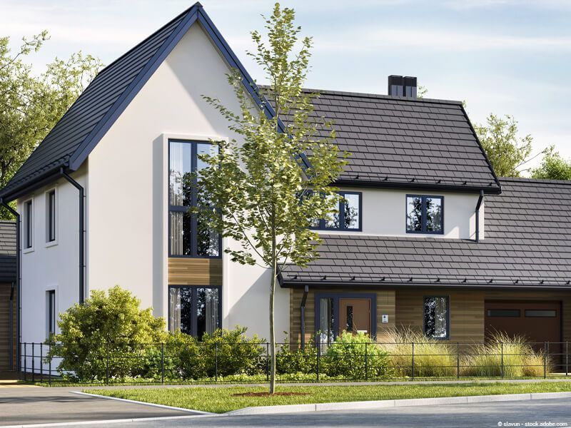 Modernes, weißes zweistöckiges Haus mit dunklem Dach, großen Fenstern und einem jungen Baum davor
