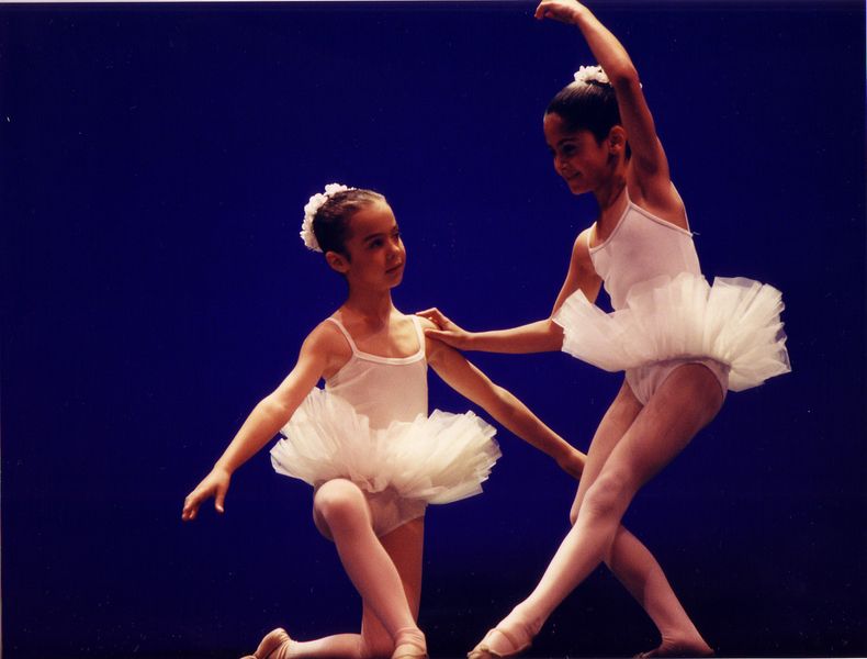 Dos chicas jóvenes con tutús blancos bailan en un escenario.