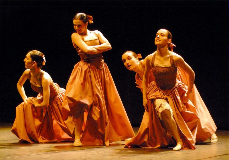 Un grupo de mujeres con vestidos naranjas bailan en un escenario.