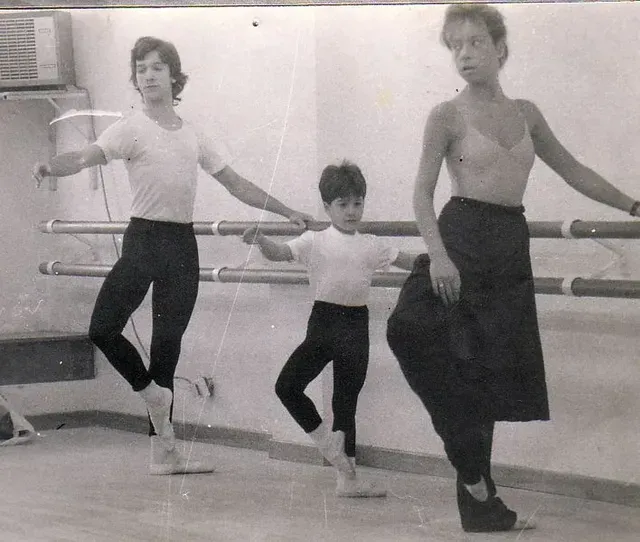 Tres personas en un estudio de ballet, practicando posturas en la barra.
