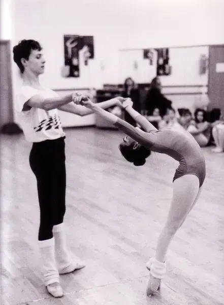 Una bailarina de ballet se arquea hacia atrás, sostenida por su compañera en un estudio de danza.