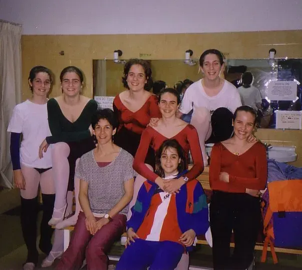 Grupo de ocho bailarines en un camerino, vestidos con leotardos y ropa deportiva.