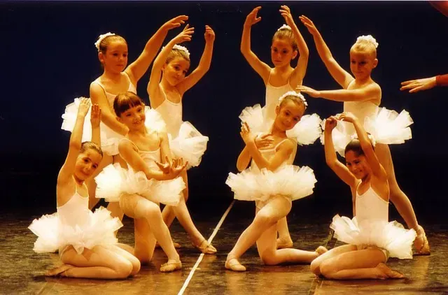 Jóvenes bailarinas de ballet con tutús y leotardos blancos actúan en el escenario con los brazos en alto.