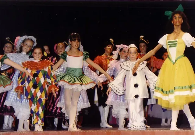 Bailarinas de ballet con coloridos trajes en el escenario, con los brazos extendidos.