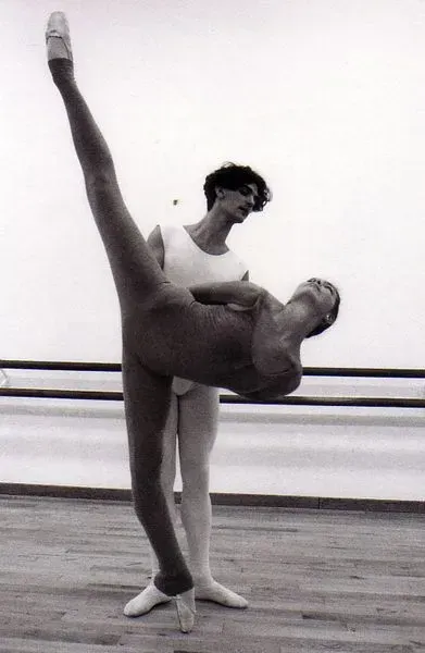 Dos bailarinas de ballet practicando una extensión de pierna alta en un estudio de danza.