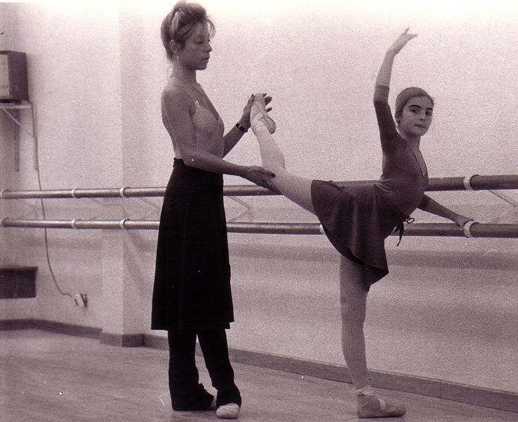Una mujer está ayudando a una joven bailarina a estirar la pierna.