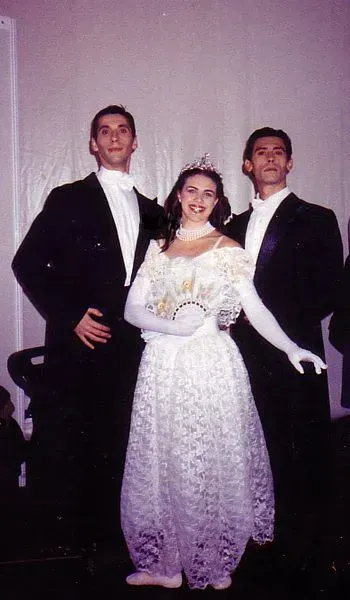 Mujer con vestido de gala blanco junto a dos hombres con esmoquin, posando.