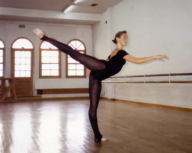 Bailarina de ballet con leotardo y mallas negras, haciendo equilibrio sobre un pie, con la pierna extendida y los brazos extendidos en el estudio.