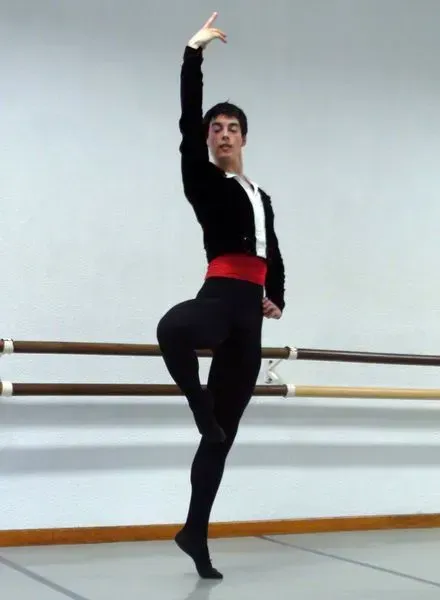 Bailarina de ballet con traje negro, fajín rojo y brazo levantado; practicando en un estudio.