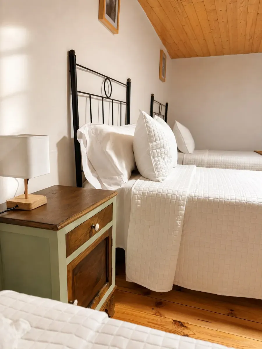 Habitación luminosa con cama de metal negro, ropa de cama blanca, mesita de noche de madera y suelos de madera cálida.