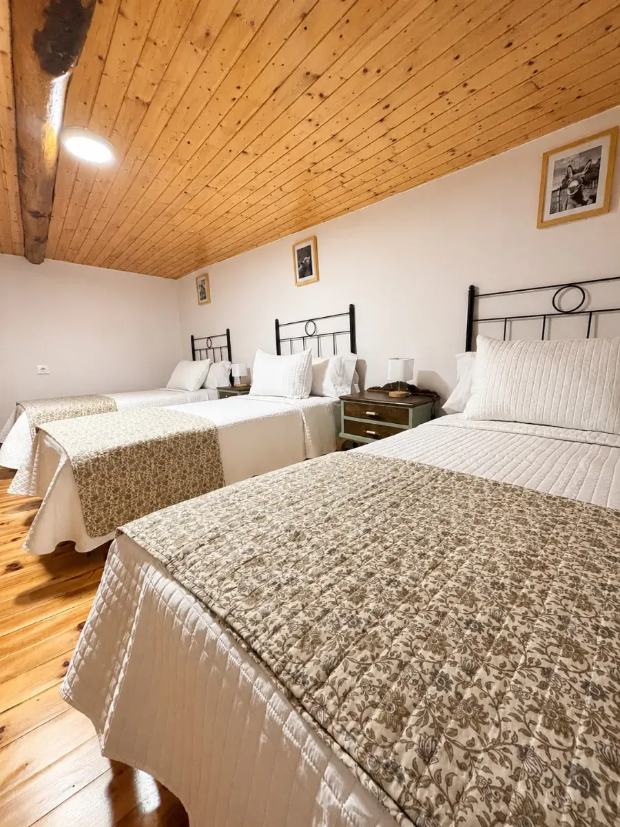 Acogedora habitación abuhardillada con dos camas individuales, sábanas blancas y techo inclinado revestido de madera.