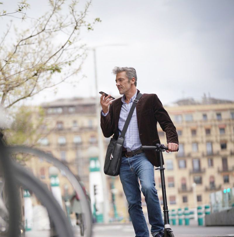 Ammattilainen seisoo sähköpotkulaudan kanssa kadulla ja pitää älypuhelinta korvallaan.