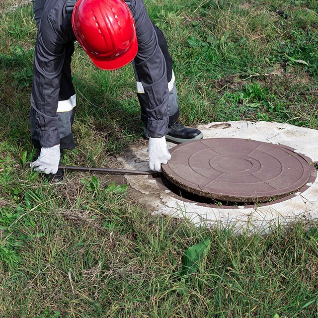 Un technicien spécialisé dans l'assainissement soulevant une plaque d'égout