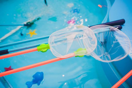 Gafas transparentes y coloridos trajes de baño flotando en agua azul, con un nadador borroso al fondo.