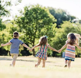 Tres niños se toman de la mano y corren en un campo.