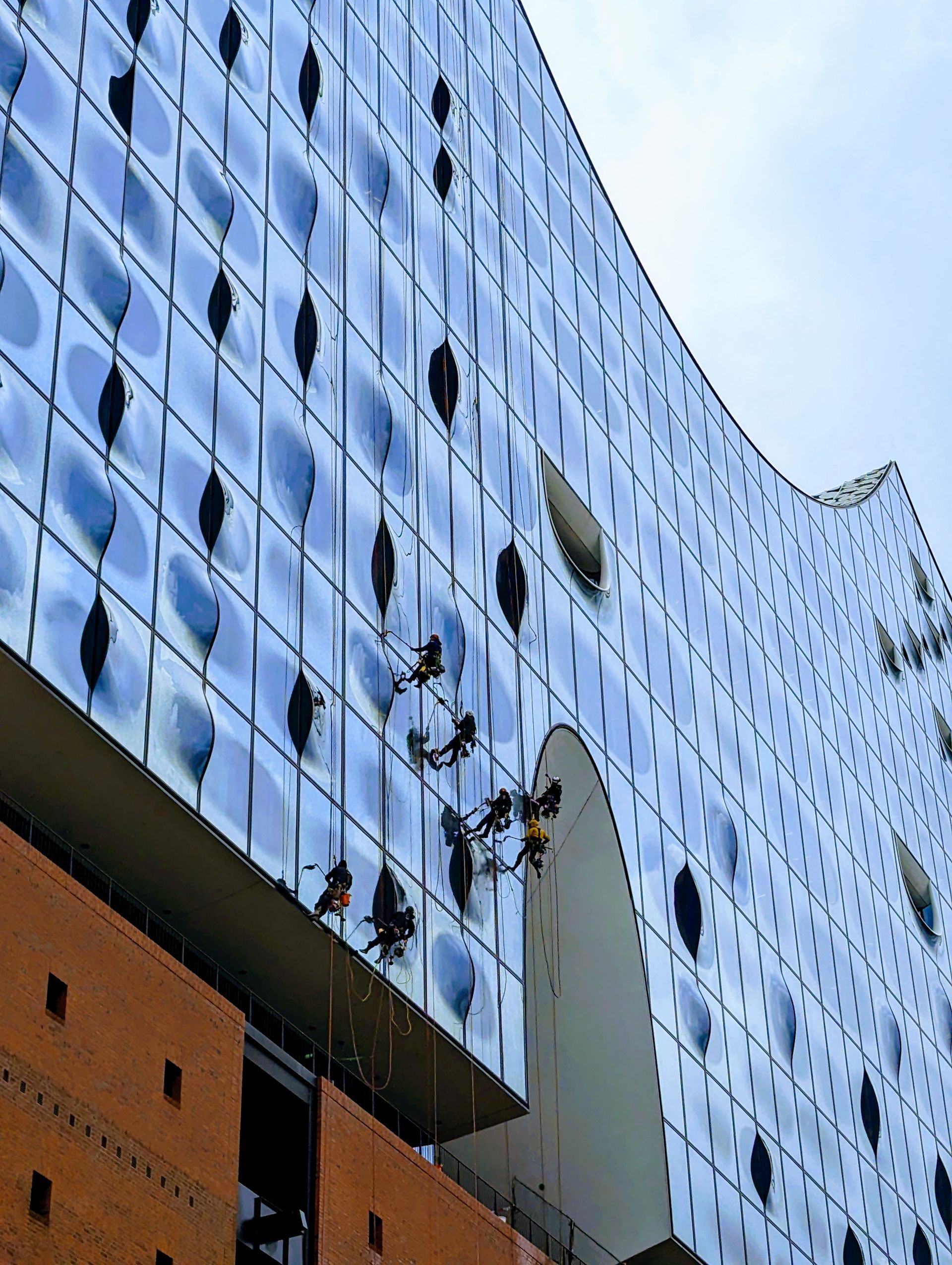 Menschen reinigen die Außenfassade der Elbphilharmonie in Hamburg, einem modernen Gebäude mit Glasfassade.