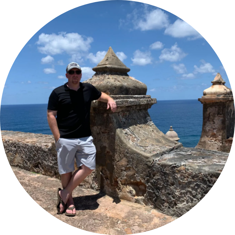 A man is leaning against a stone wall overlooking the ocean.