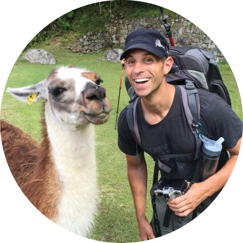 A man with a backpack is standing next to a llama.