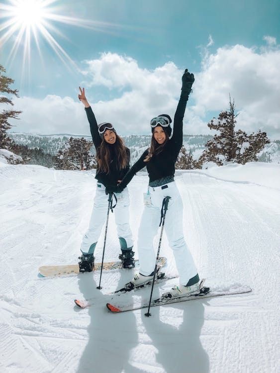 Two women are standing on skis and snowboards in the snow.