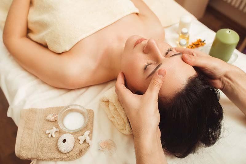 Mujer recibiendo un masaje facial en un spa, con las manos en la frente y expresión relajada.
