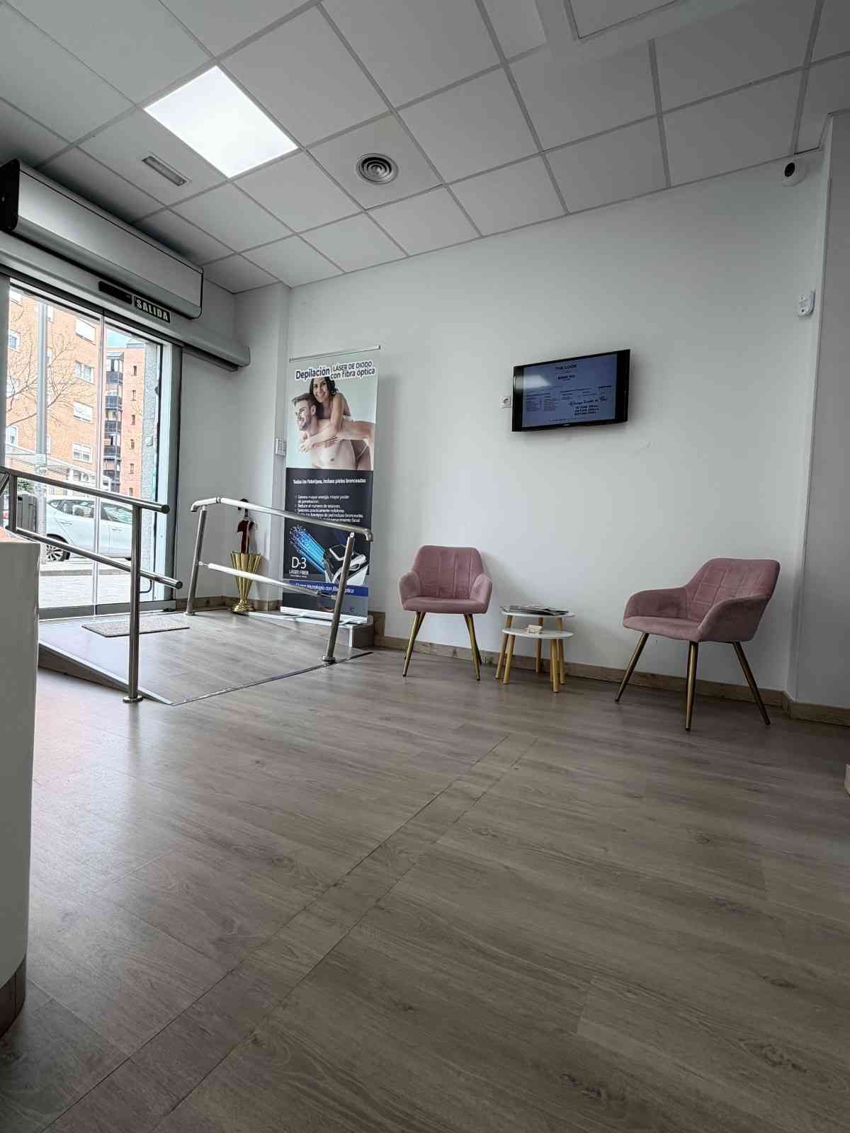 Una sala de espera con dos sillones de color rosa claro, una pequeña mesa auxiliar, un televisor.