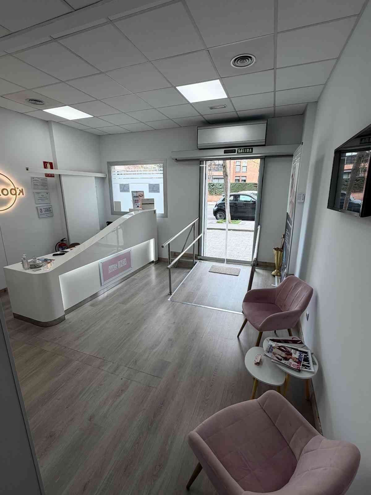 Moderna zona de recepción de oficina con un escritorio blanco, dos sillas rosas, suelo con aspecto de madera.