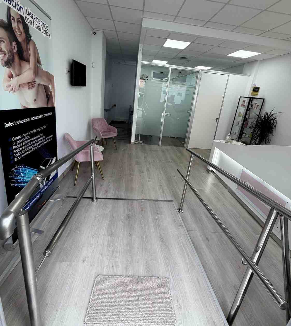 Un espacio interior luminoso con suelo de madera clara, dos sillas rosas, pasamanos de metal y una zona de recepción.
